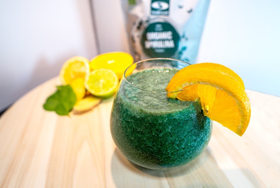 Et glas spirulina- og citrussmoothie i et glas med en skive appelsin p kanten.